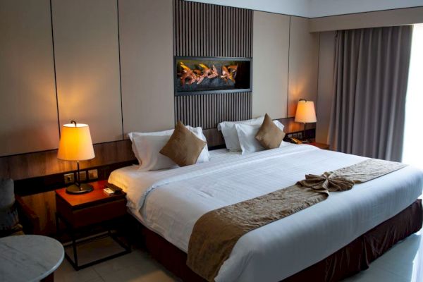 A cozy hotel room with a large bed, pillows, bedside tables with lamps, and a decorative wall feature. Neutral tones create a relaxing ambiance.