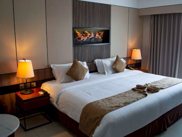 A cozy hotel room with a large bed, pillows, bedside tables with lamps, and a decorative wall feature. Neutral tones create a relaxing ambiance.