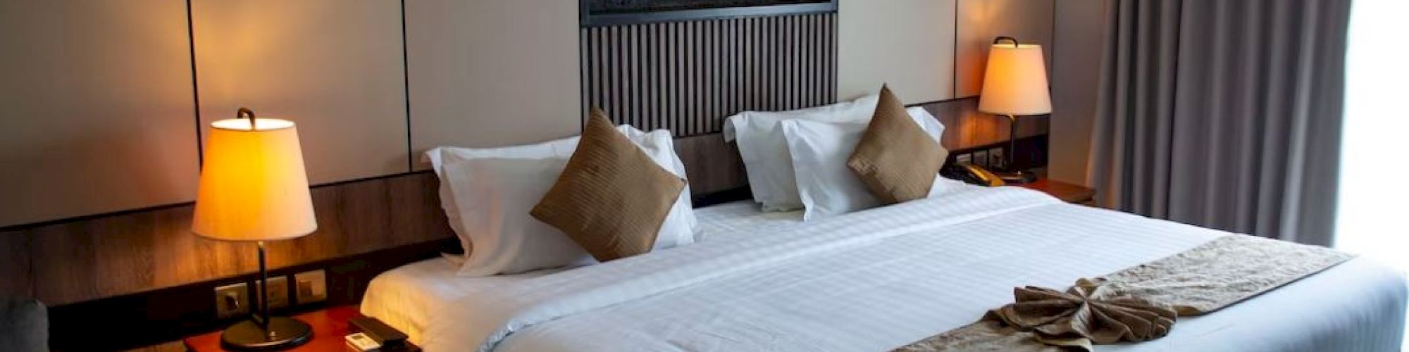 A cozy hotel room with a large bed, two bedside lamps, and art above the headboard. Modern design and neutral tones create a relaxing vibe.