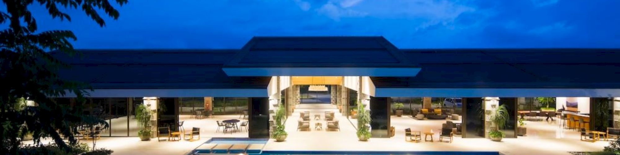 A luxurious villa with an illuminated pool at dusk, featuring modern architecture and an open, inviting interior space.