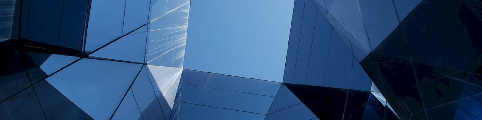 The image shows an upward view of modern glass buildings with reflective surfaces forming a geometric pattern against a blue sky.