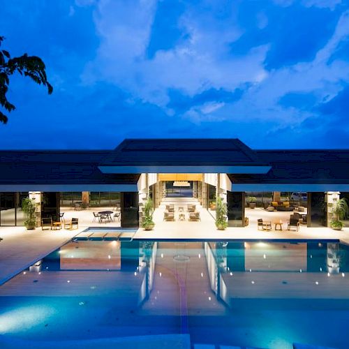 Luxurious resort with a large, illuminated pool and elegant open-air architecture under a twilight sky.