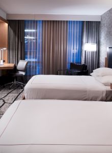 A modern hotel room with two beds, a desk, a TV, and stylish lighting and decor, giving it a comfortable and chic appearance.
