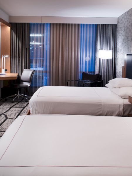 A modern hotel room with two beds, a desk, a TV, and stylish lighting and decor.