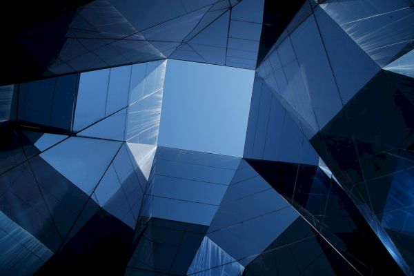 The image shows a geometric pattern of mirrored glass buildings reflecting the sky, creating an abstract architectural perspective.