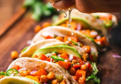 A hand squeezes lime over a row of vibrant tacos filled with chickpeas, avocado, and veggies on a wooden board.