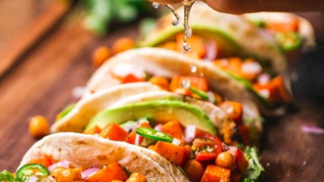 A hand squeezes lime over a row of vibrant tacos filled with chickpeas, avocado, and veggies on a wooden board.