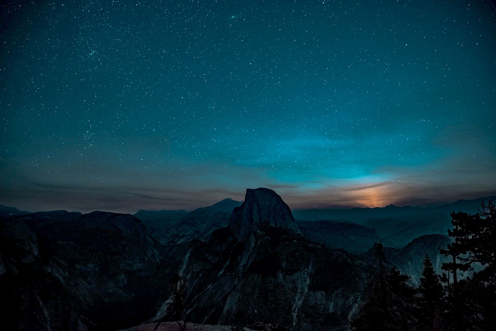 A starry night sky over a mountain landscape with a glowing horizon. The scenery is serene and picturesque, capturing a tranquil night.