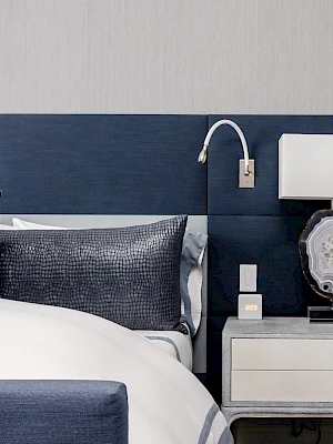 A stylish bedroom with a blue and gray theme, featuring a neatly made bed, nightstand, modern lamp, and decorative pillows.