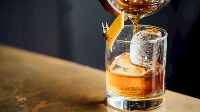 A cocktail being poured over ice in a glass, garnished with a twist of citrus peel.