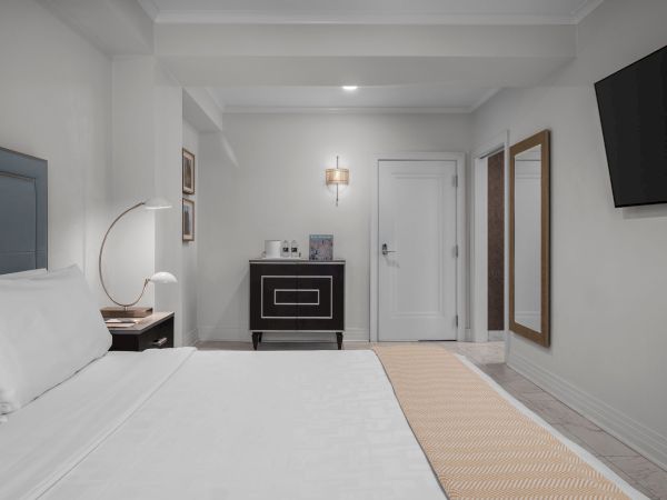 A modern hotel room with a neatly made bed, a TV on the wall, a side table, a cabinet, and a minimalist decor.