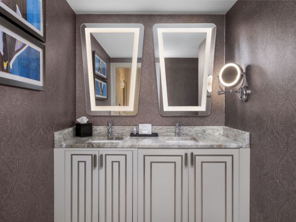 A modern bathroom with dual sinks, rectangular mirrors, wall art, and elegant textured wallpaper.