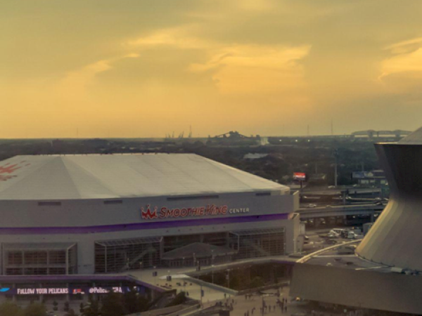 An arena is shown with a parking lot and a distinctive circular structure nearby under a cloudy sky at dusk.