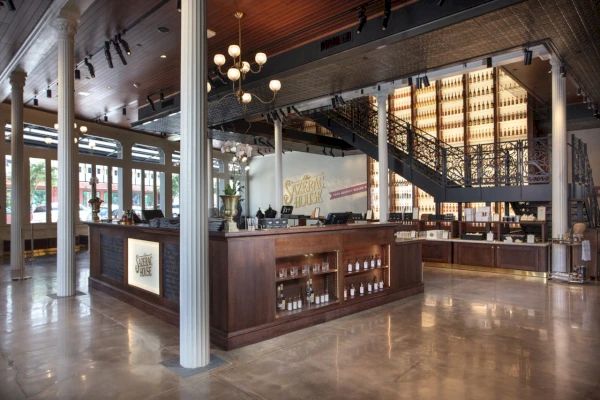 An elegant whiskey distillery interior with wooden counters, bottles on display, a staircase, and stylish lighting features the branding.