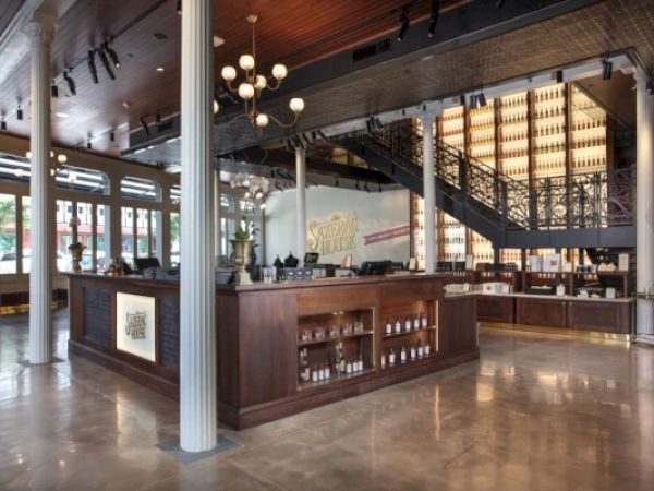 An elegant whiskey distillery interior with wooden counters, bottles on display, a staircase, and stylish lighting features the branding.
