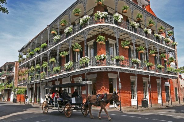 A horse-drawn carriage passes a charming, historic building adorned with greenery and ornate ironwork on its balconies.