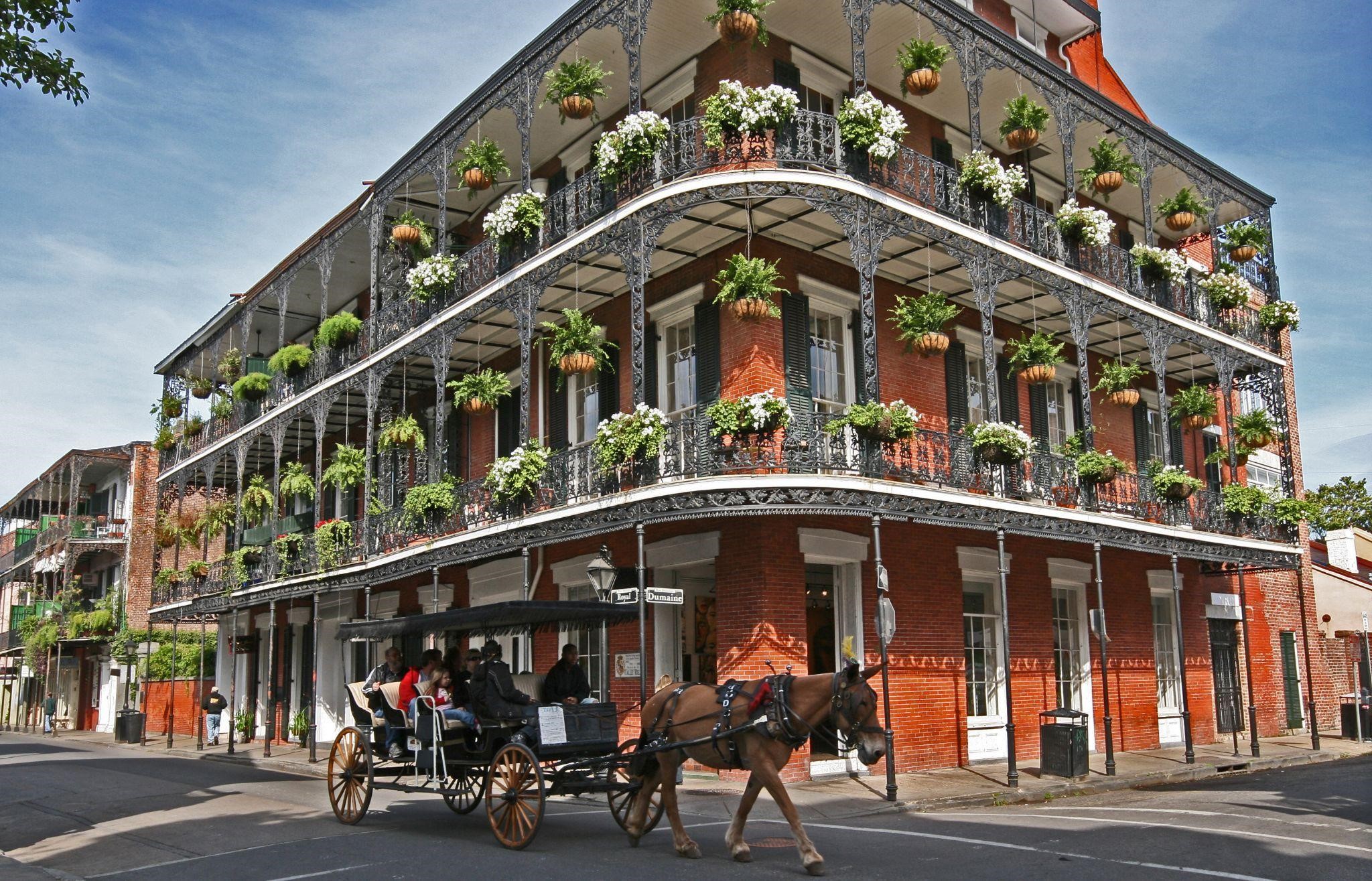 A red brick building with balconies and plants, with a horse-drawn carriage in front.