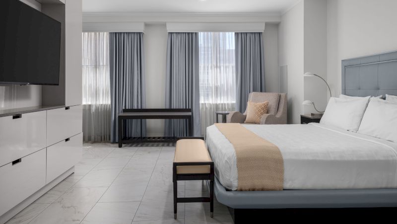 A wide view of a hotel room with a large bed, desk, TV, and window