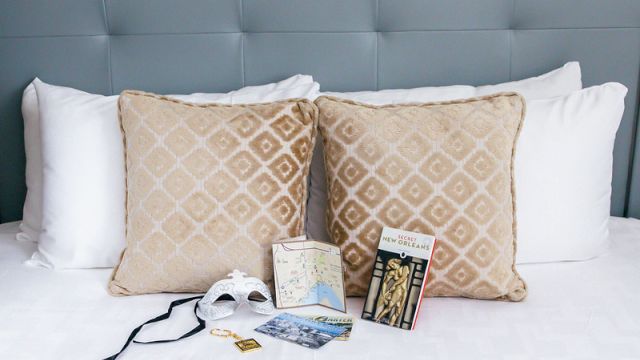A neatly made bed with patterned pillows and a tufted headboard, with brochures and a mask on the bed.