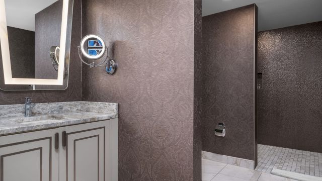 A bathroom with a marble countertop, shower, sink, and mirror