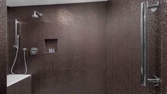 A brown tiled shower with silver fixtures and a bench.