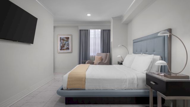 A hotel room with a bed, nightstand, TV, window, and chair.