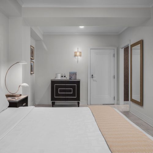 A tidy hotel room featuring a neatly made bed, a wall-mounted TV, and minimalist decor, creating a modern and comfortable ambiance.