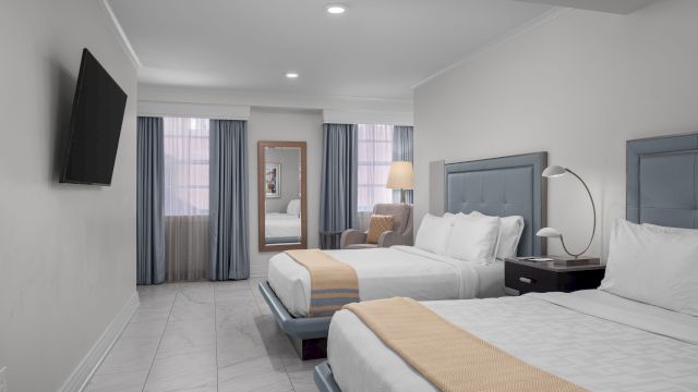 A wide view of a hotel room with two beds, a TV, and a mirror.