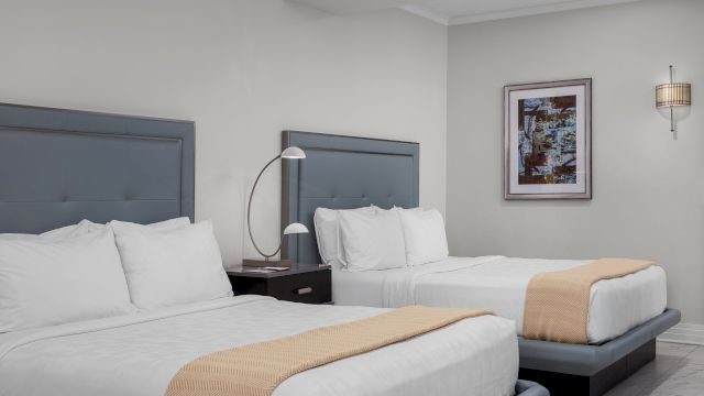 A hotel room with two beds, a nightstand, and artwork on the wall.