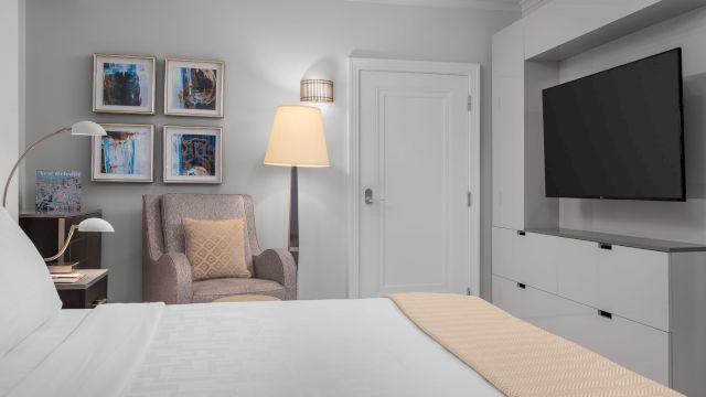 A wide view of a hotel room with a bed, chair, TV, and artwork on the wall.