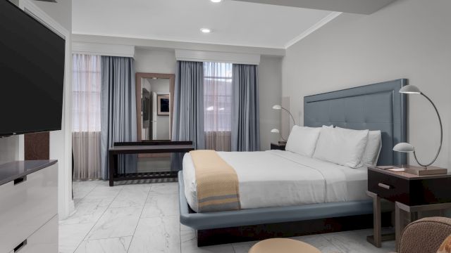 A wide view of a hotel room with a bed, TV, desk, and mirror