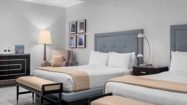 A wide view of a hotel room with two beds, a tiled floor, and modern furnishings.