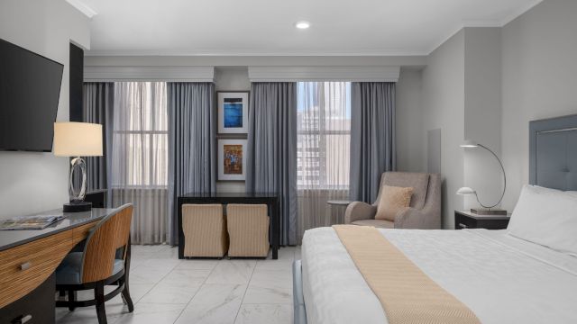 A wide view of a hotel room with a bed, desk, chair, and window.