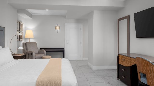 A hotel room with a bed, desk, chair, and TV.