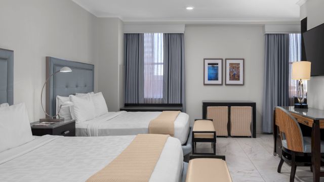 A hotel room with two beds, a desk, and a TV.