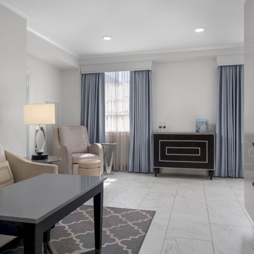 A modern living room with light-colored furniture, a table, and wall art. A TV is mounted on the wall.