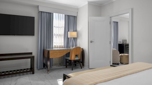 A wide view of a hotel room with a bed, desk, TV, and mirror.