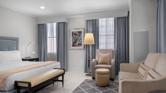 A wide view of a hotel room with a bed, sofa, chair, and lamp