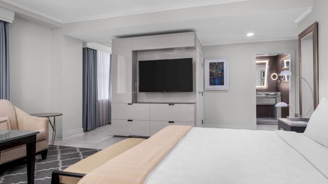 A wide view of a hotel room with a bed, TV, sofa, and bathroom in the background.