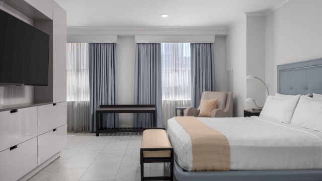 A wide view of a hotel room with a bed, TV, desk, chair, and window.
