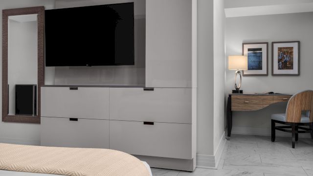 A hotel room with a bed, desk, chair, TV, and mirror