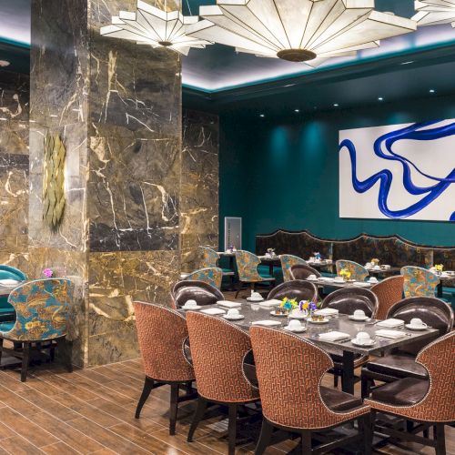 Elegant dining area with patterned chairs, marble columns, abstract wall art, overhead lighting, set tables with cups and saucers, floral decor.