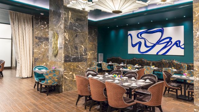 A dining area with tables and chairs, marble columns, and artwork on the wall.