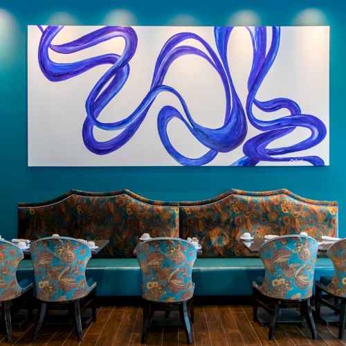 A teal room with a set of patterned chairs and a bench under a blue abstract artwork on the wall, creating a stylish atmosphere.