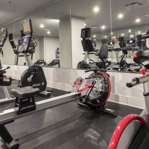 The image shows a gym with exercise bikes, a rowing machine, and mirrors on the walls.