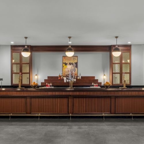 A large wooden bar with hanging lights, a decorative painting, and shelves with bottles behind it in a modern setting.