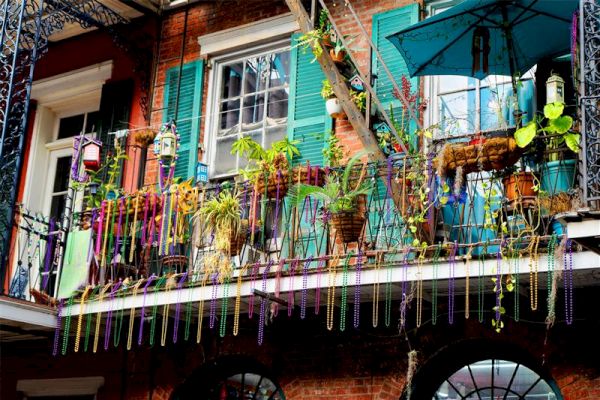 A balcony decorated with colorful beads, plants, and vibrant shutters, suggesting a festive atmosphere.