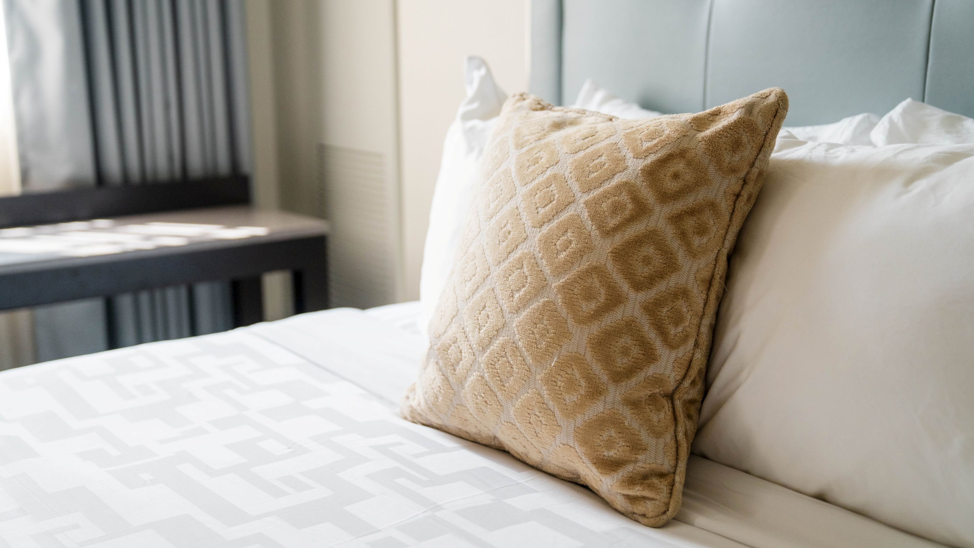 A close-up of a bed with white sheets and a tan pillow