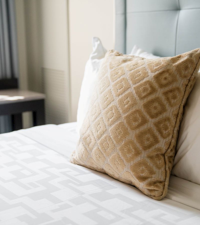 a close-up of a bed with a white sheet, a tan and white patterned pillow, and a light blue headboard