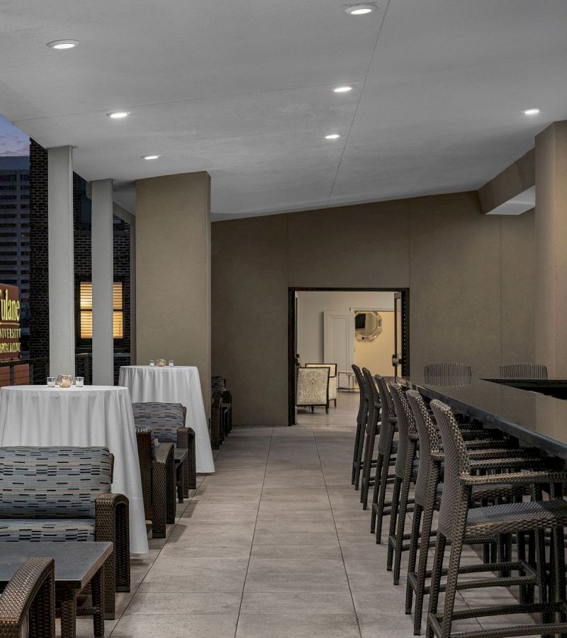 A dimly lit bar with wicker chairs and white tablecloths.